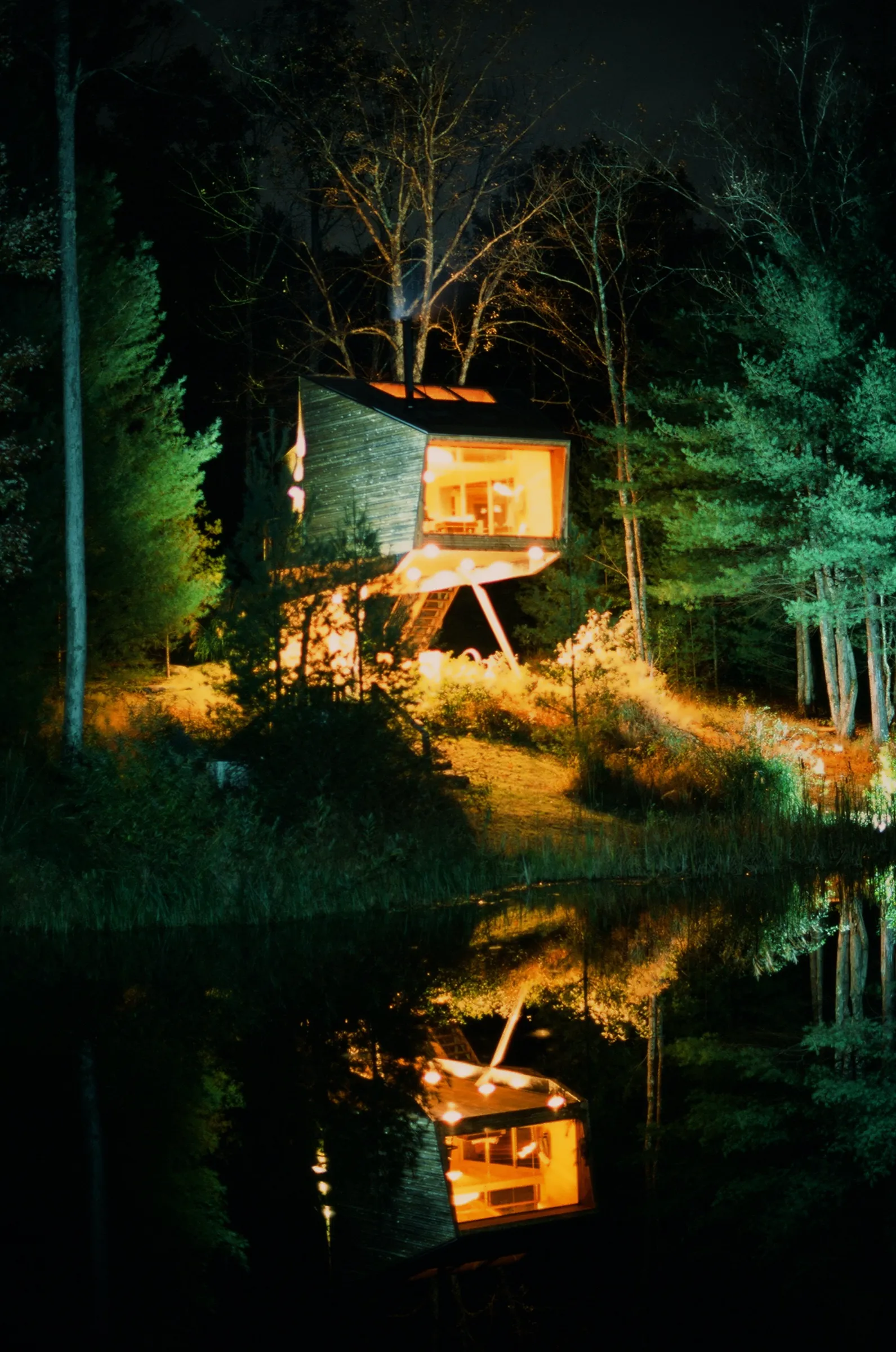 Treehouse glowing at night reflected in pond