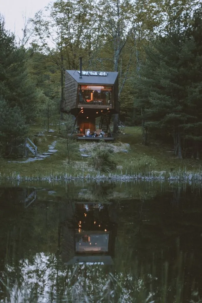 Willow Treehouse glowing at summer dusk, reflected in the pond